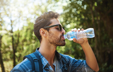 Staying hydrated on his hike. Shot of a young man stopping for a drink of water while exploring the...