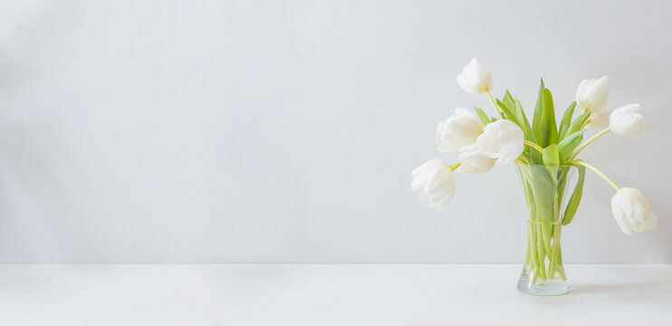 White spring tulips in a vase on a white table. Mock up for displaying works