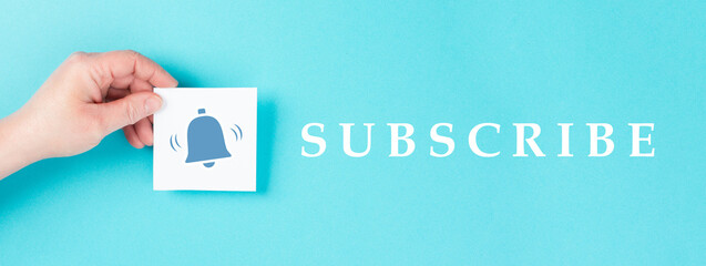 Subscripe is standing on a blue colored background, hand holds a paper with a bell symbol, social...