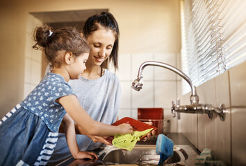 Good job my lovely girl. Shot of a happy little girl and her mother washing the dishes together at home.