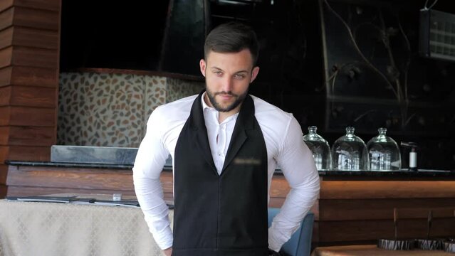 Happy young waiter happily putting on an apron and getting ready for the working day. Waiters put on their uniforms before starting work. Customer service in an elite restaurant