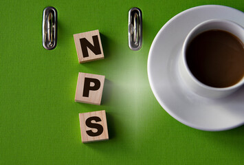 NPS - acronym on wooden cubes against the background of a green folder and a cup of coffee