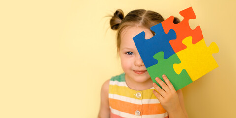 A cute beautiful blue - eyed girl holds an autism symbol in hand, covering her face with it and...