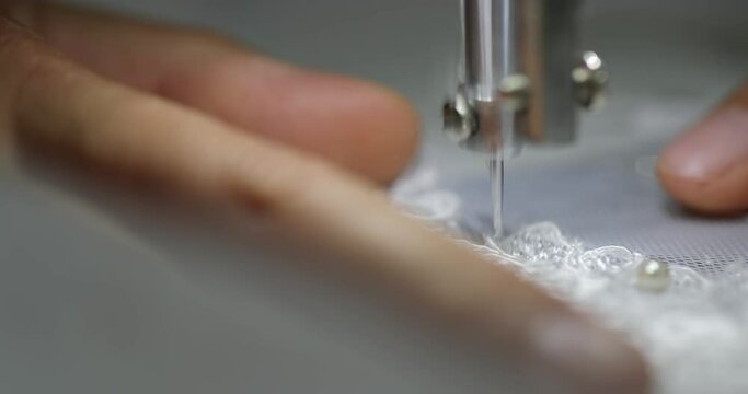 female hands of a seamstress with the help of a needle foot of a sewing machine embroiders a flower pattern on a white fabric of a wedding dress. macro