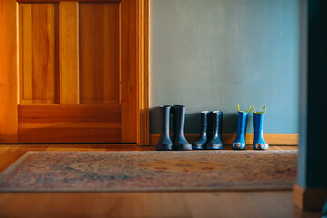 Fototapeta na wymiar Three pairs of blue rainboots are lined up against a wall next to a door