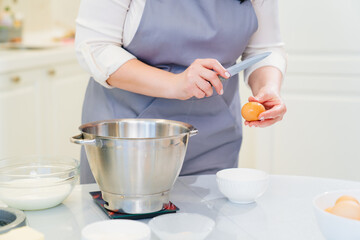 A woman breaks an egg with a knife to prepare cream or dough in a mixer bowl.