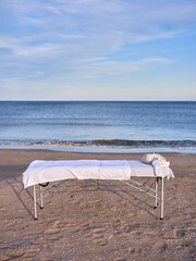 Fototapeta na wymiar Front view of a massage table placed on the sand of a beach with the sea in the background.