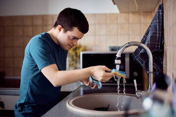 Young down syndrome man washing dishes under the kitchen sink.