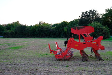 red agricultural machinery, plow, harrow for tillage in the field after harvest, green trees in the background, modern crop cultivation concept