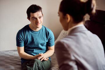 Smiling man with down syndrome enjoys in conversation with psychologist at home.
