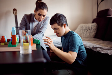 Young down syndrome man and his psychologist use toy blocks during home visit.
