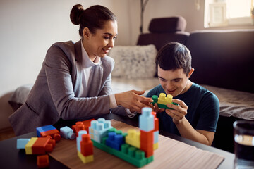 Happy man with down syndrome and his psychologist play with toy blocks at home.
