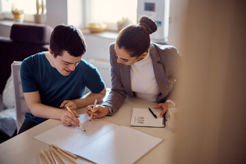 Happy down syndrome man and his psychologist drawing together on paper during home visit.
