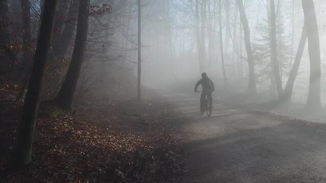 Single mountain biker riding in epical moment with sun rays shining through fog, going uphill towards the sun. Epic MTB ride.
