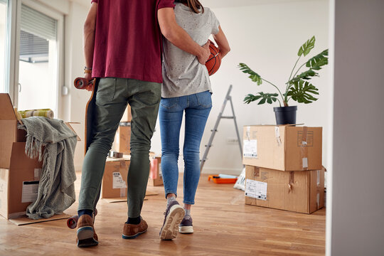 cropped image of young couple from behind holding  each other, walking in new apartment with unpacked boxes around them