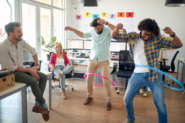 A group of employees is having fun while playing with hula-hoop in the office. Employees, job,...
