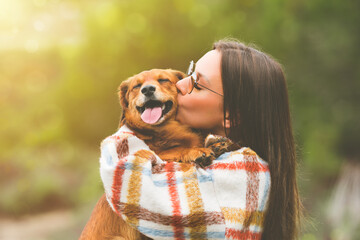 Beautiful woman hugging and kissing dog. Dog and owner together outdoors. Love and friendship between dog and owner - Powered by Adobe