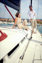 A young couple is chatting and enjoying the sun on a yacht while riding on the seaside. Summer, sea, vacation, relationship