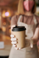 Close-up selective focus on foreground shot of unrecognizable waitperson wearing mask and gloves giving cup of coffee to customer