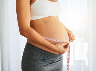 Body designed by baby. Cropped shot of a pregnant woman measuring her belly at home.