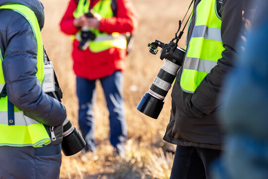 Group Of Many People Watching Planes Landing And Take Off Airport Runway Field Planespotting Conference Warm Morning Time. Planespotters In Safety Vest Waiting Aicraft Arrival Approaching Departure