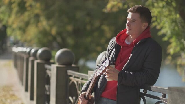 Street lifestyle. Coffee to go. Outdoor leisure. Thoughtful dreamy man enjoying sunny autumn weather drinking latte takeaway at park embankment copy space.