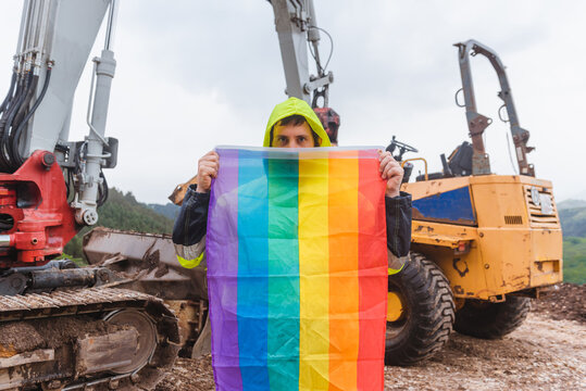 Working Man On A Construction Site Holding A Rainbow Lgbt Pride Flag Demanding Equal Treatment At His Job. Concept Of Sexual Discrimination In Employment.