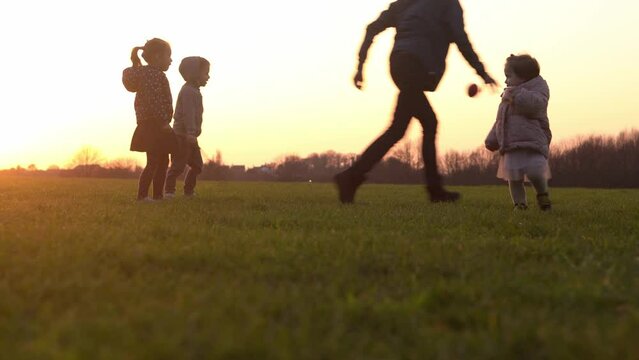 Happy family at sunset. Silhouette of group of people walk in park. child with parents holding hand. Father playing football game on grass. Young Dad fave fun do sport with children siblings outside