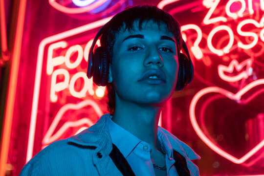 Neon light portrait of bearded smiling man in headphones, sunglasses, white t-shirt. Listening to music