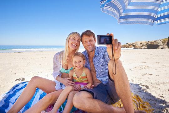 Smiling for a holiday pic. Shot of a happy young family taking a photo of themselves at the beach.