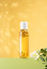 Fresh jasmine flowers inside a bottle of jasmine essential oil standing on a light green podium. Cosmetic oil for body baths on an yellow background. Phytotherapy, aromatherapy, antistress, self-care