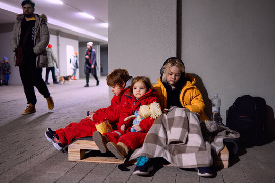 Group Of Little Kids, Siblings Sitting Quietly On Wooden Pallet On The Floor In Bomb Proof Shelter During Air-raid Attack. Russian Invasion To Ukraine