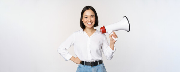Smiling young asian woman posing with megaphone, concept of news, announcement and information,...