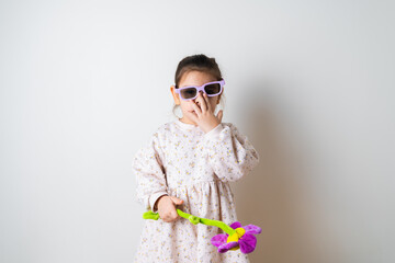 Toddler girl in sunglasses play with toy flower on white background