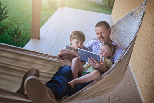 Swinging along to a chilled weekend with the kids. Shot of a father and his two little children using a digital tablet while relaxing on a hammock outdoors.