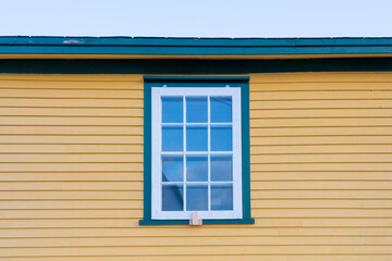 The exterior of a vintage yellow and green colored exterior wall with narrow wood cape cod clapboard siding. In the center of the house, there's a closed single hung window with a mountain reflection. - obrazy, fototapety, plakaty