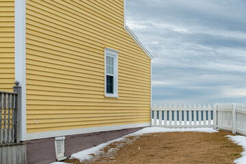 A yellow country style wooden building with a white picket fence attached and enclosing the...