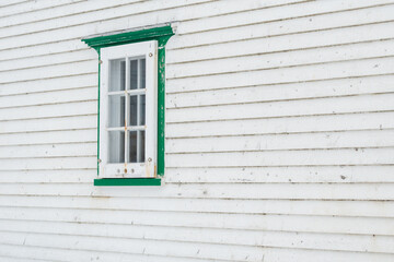 A small single casement window in a white narrow wood beveled clapboard siding exterior wall of a...
