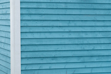 The exterior of a bright blue narrow wooden horizontal clapboard wall of a house. The trim on the building is white in color. The outside boards are textured pine wood. The vintage building is clean.