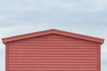 The exterior of a red wooden clapboard building with a peaked roof. The wood wall is horizontal cape cod beveled clapboard siding. The background is blue sky with white clouds. 