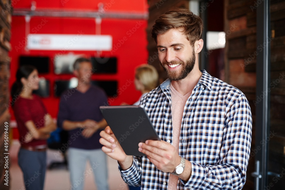 Poster enjoying his new work tool. shot of a young designer using a tablet with her colleagues standing in 