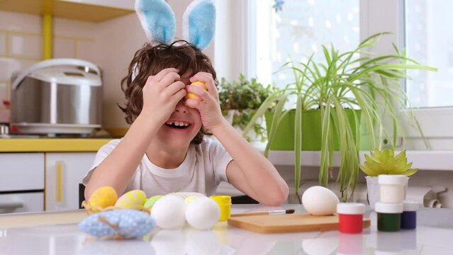 dyeing Easter eggs. curly boy dressed in white Tshirt and blue bunny ears paints Easter eggs. FullHD 24 FPS