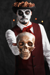 Day of the Dead. Cropped portrait of a handsome young man dressed in his Mexican-style halloween costume holding out a skull.