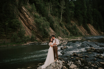 Elegant gentle stylish bride and groom by the river with stones in the mountains. A loving wedding couple.