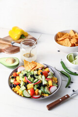 Bowl of Mexican vegetable salad and ingredients on light wooden background