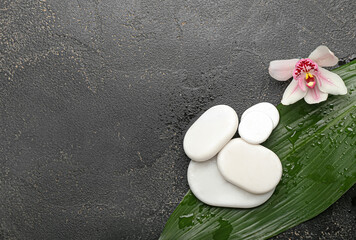 Fototapeta na wymiar Spa stones with orchid flower and tropical leaf on dark background