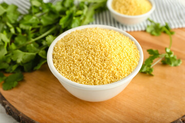 Bowl of raw couscous with parsley on table, closeup