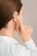 Young woman with hearing aid in her ear on grey background, closeup