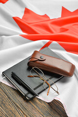 Notebook with pen, eyeglasses and Canadian flag on dark wooden background