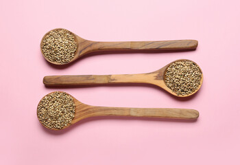 Spoons with hemp seeds on color background